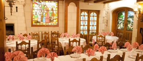 Un comedor con mesas redondas, sillas de madera y servilletas rosas.