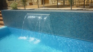 Zwembad met een waterval, omringd door een stenen muur en een metalen hek.