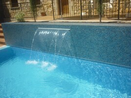 Piscina com cascata, cercada por um muro de pedra e uma grade de metal.
