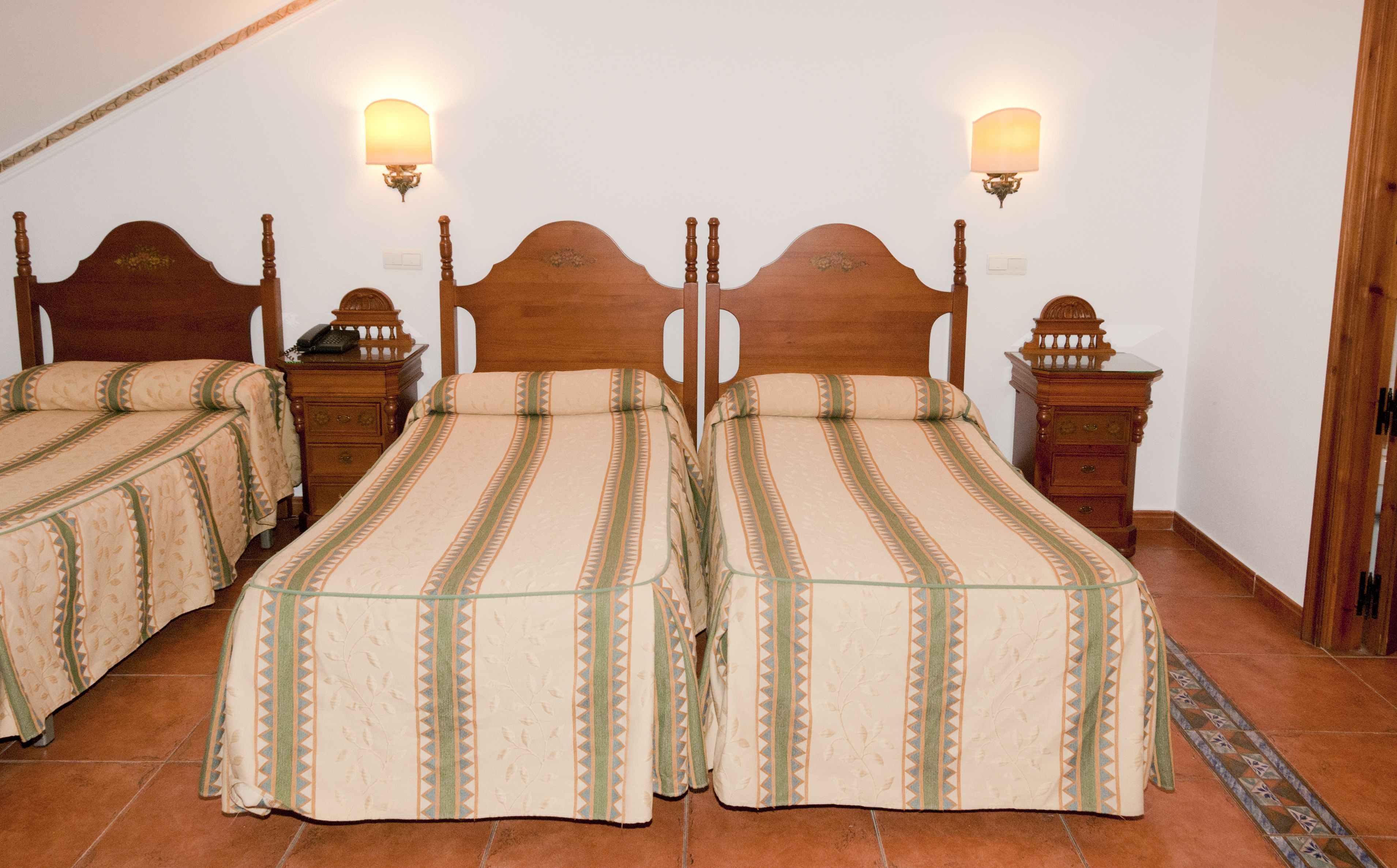 A room with two wooden beds, each with a headboard and footboard, and two bedside tables with lamps.