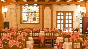Een feestzaal met rijen tafels, elk gedekt met witte tafelkleden en roze stoelhoezen, klaar voor een formeel evenement.