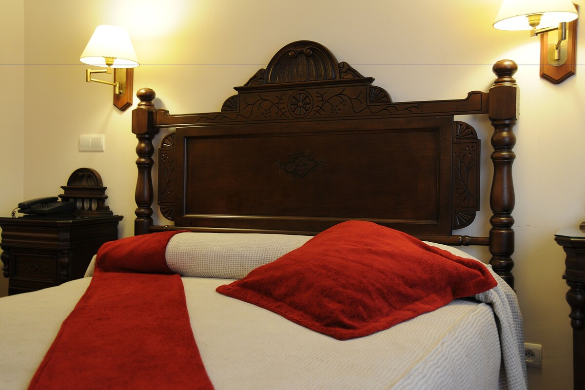 A bed with a wooden headboard, two wall-mounted lamps, and a telephone on a nightstand.