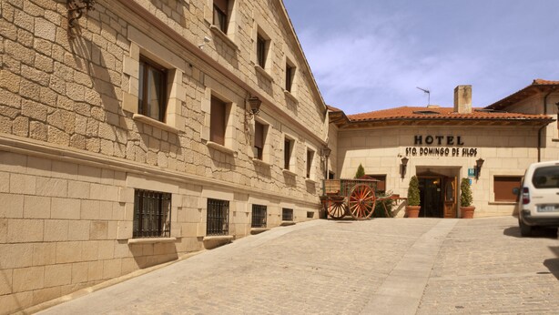 A historic building with a stone facade, a sign reading "HOTEL St. Domingo de Silos," and a traditional carriage parked in front.
