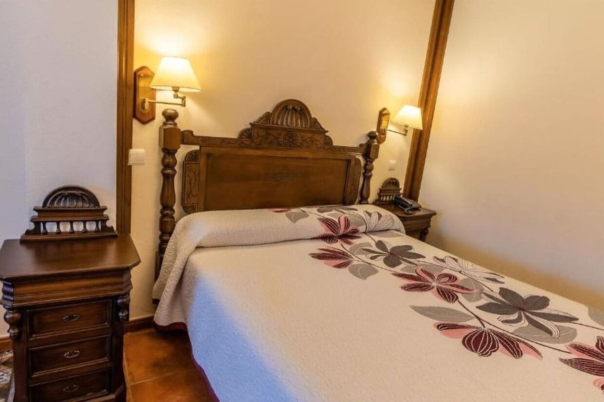 A bedroom with a wooden bed frame, two bedside lamps, a nightstand, and a floral bedspread.