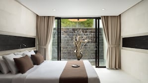 Una habitación de hotel moderna con una cama grande, vista a una cascada a través de puertas de vidrio y una pared de piedra.
