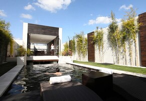 Un espace piscine extérieur moderne, doté d’un design minimaliste, entouré de murs en bois et de plantes en bambou.