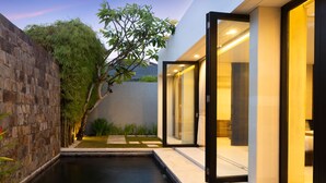 A modern outdoor pool area with a stone wall, a tree, and a glass-enclosed spa room. - eqUILIBRIA SEMINYAK (Keroboken Kelod)