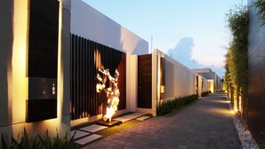 A modern building with a fire feature, a pathway, and a row of plants. - eqUILIBRIA SEMINYAK (Keroboken Kelod)
