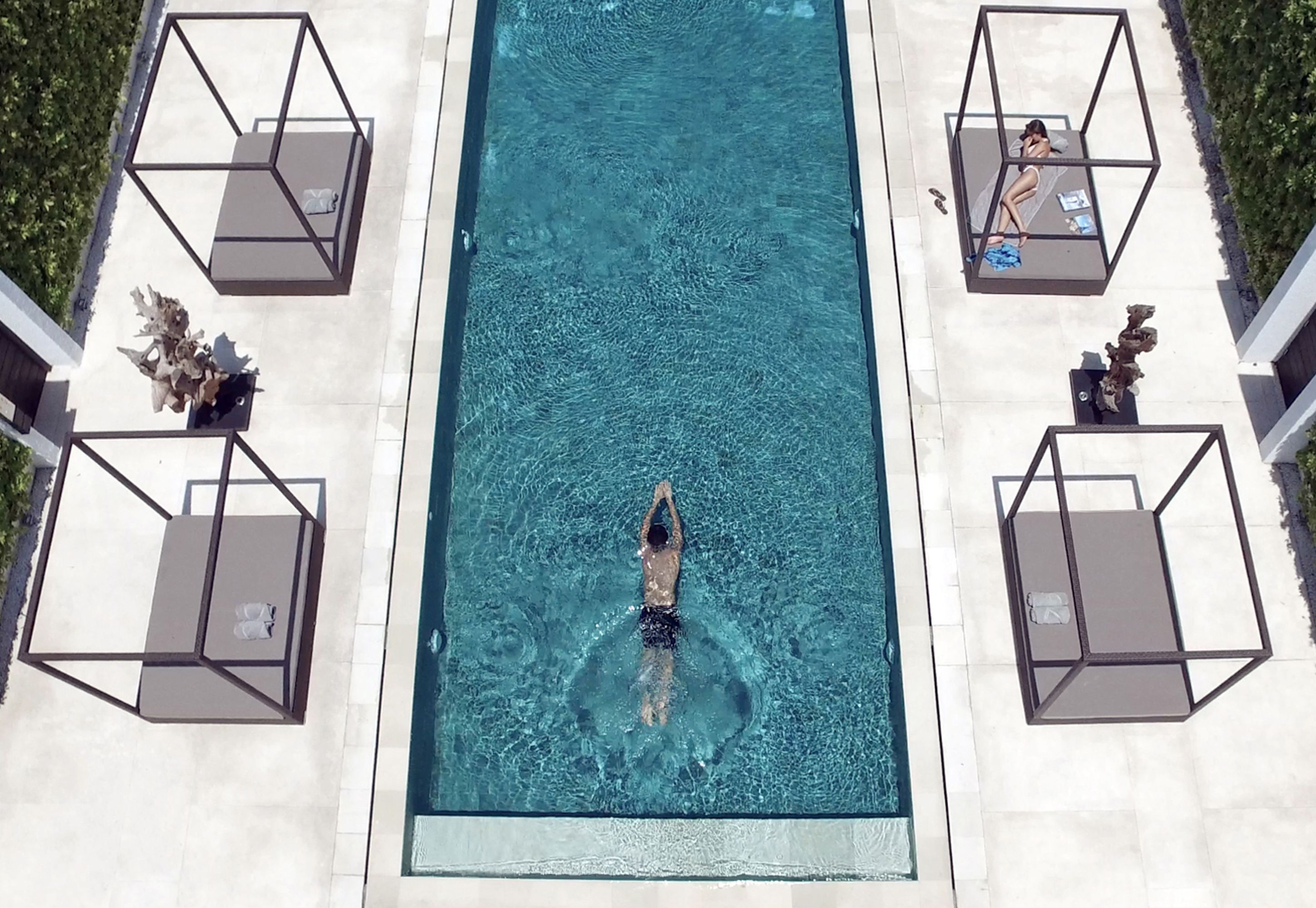 A rectangular swimming pool with a person swimming, surrounded by lounge chairs and a clear sky.