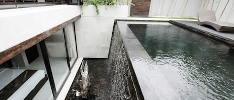 A modern outdoor pool area with a built-in bench and a small waterfall feature.