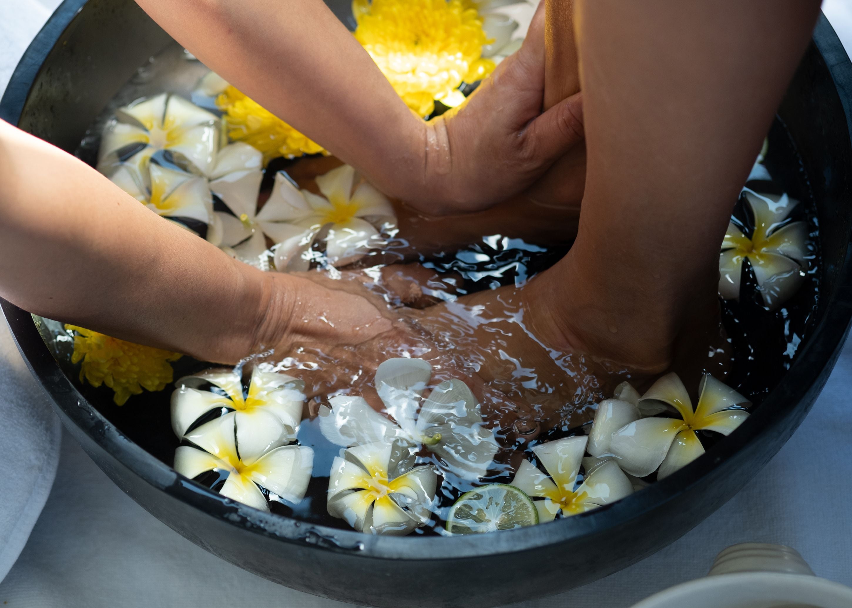 Hands submerged in water with flowers and slices of lime.