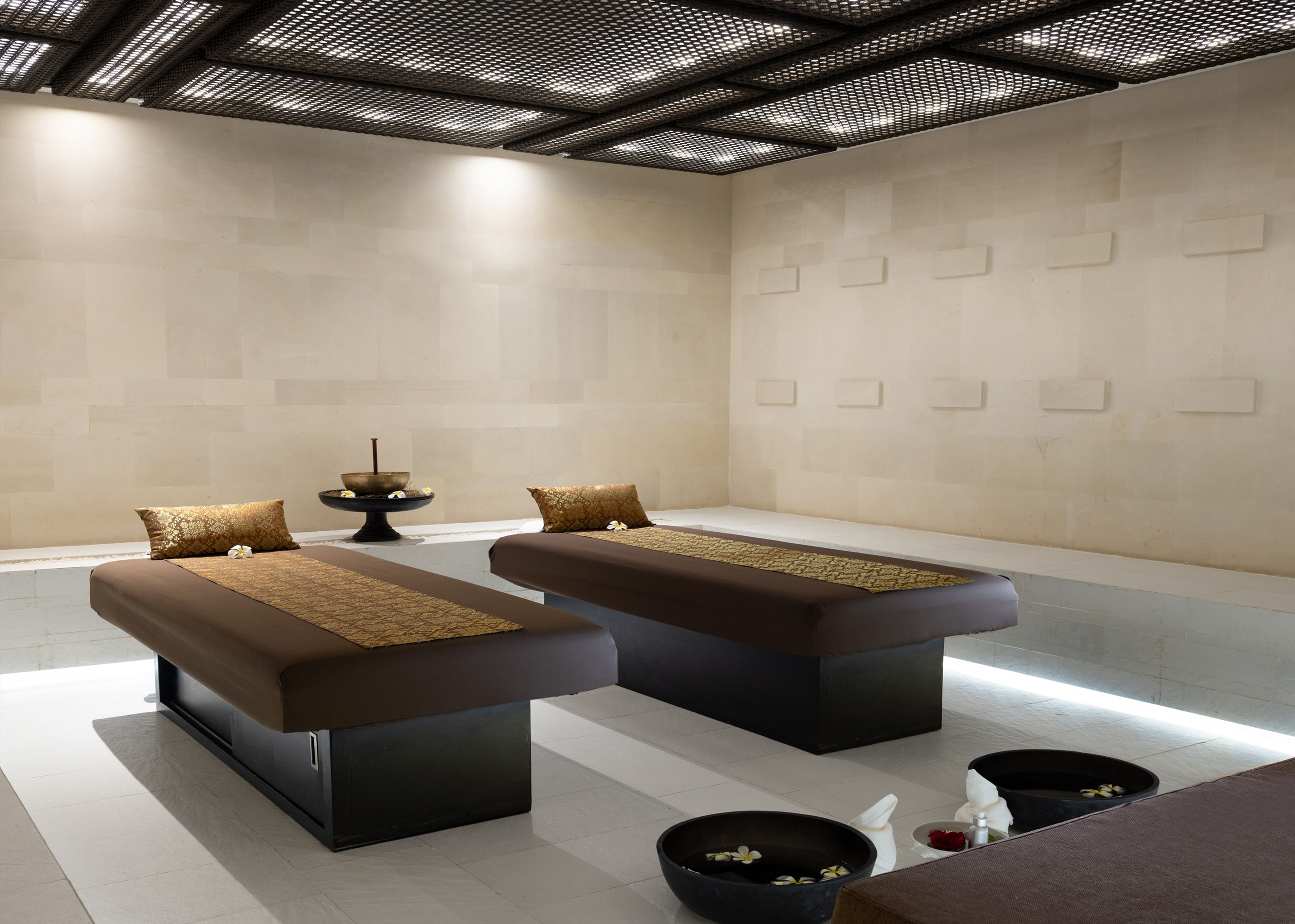 Un moderno spa con dos camillas de masaje, un cuenco decorativo con flores y una pequeña fuente.