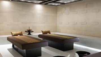 Un moderno spa con dos camillas de masaje, un cuenco decorativo con flores y una pequeña fuente.