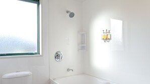 Un baño con una bañera blanca, un inodoro, un cabezal de ducha y una ventana.