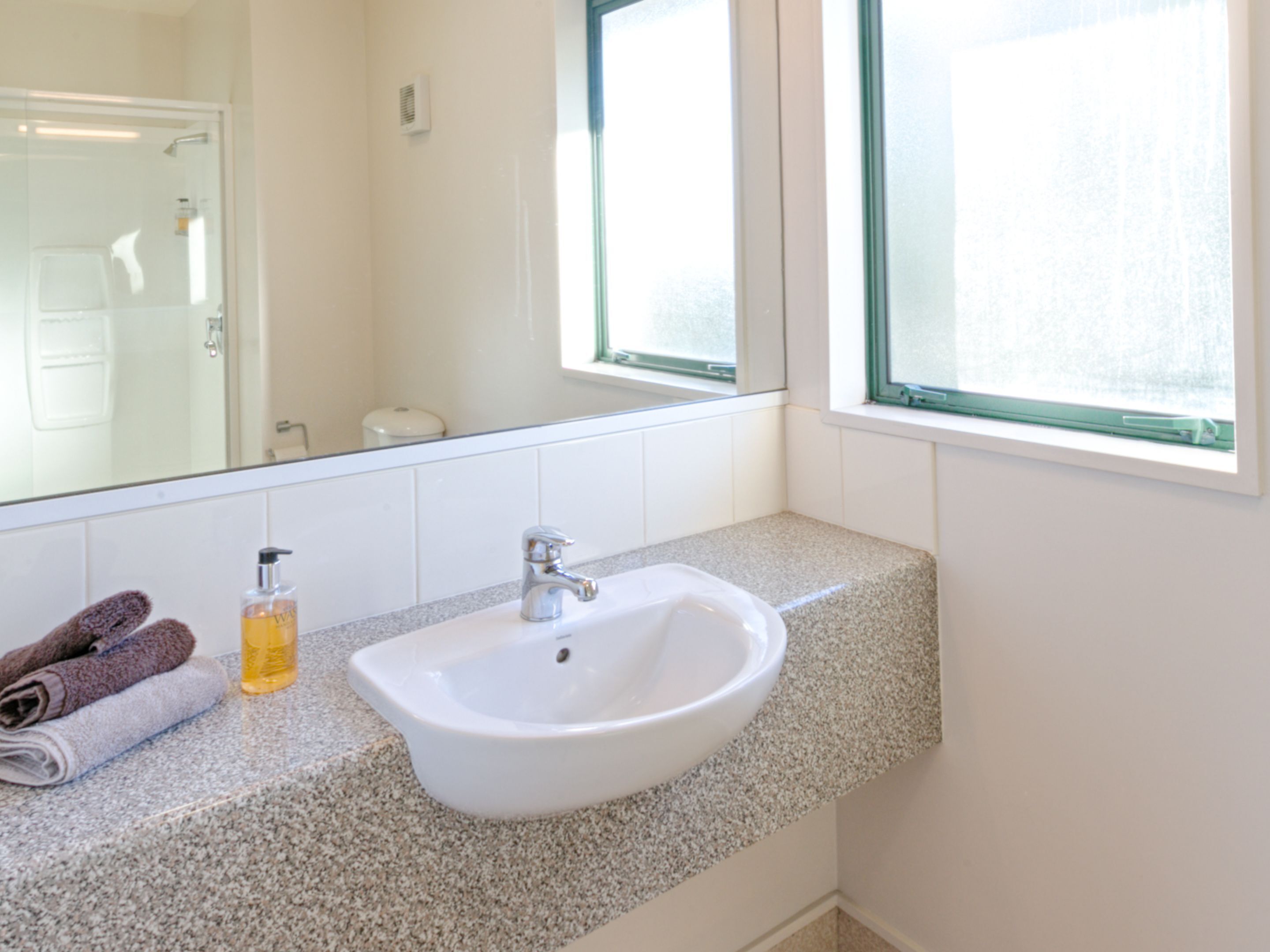 Un baño con un lavabo blanco, un espejo y una ventana.