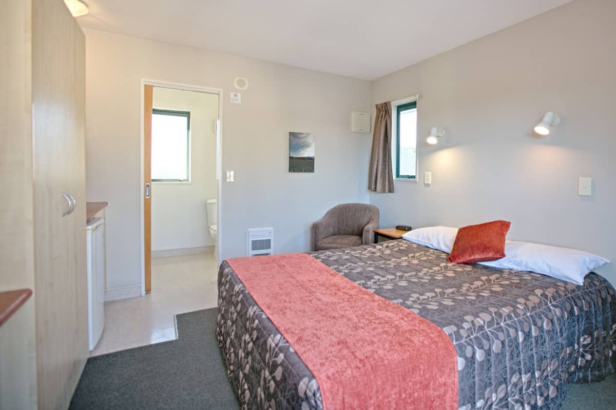 Ein Hotelzimmer mit zwei Betten, einem Sessel, einem kleinen Tisch und einem Fenster.
