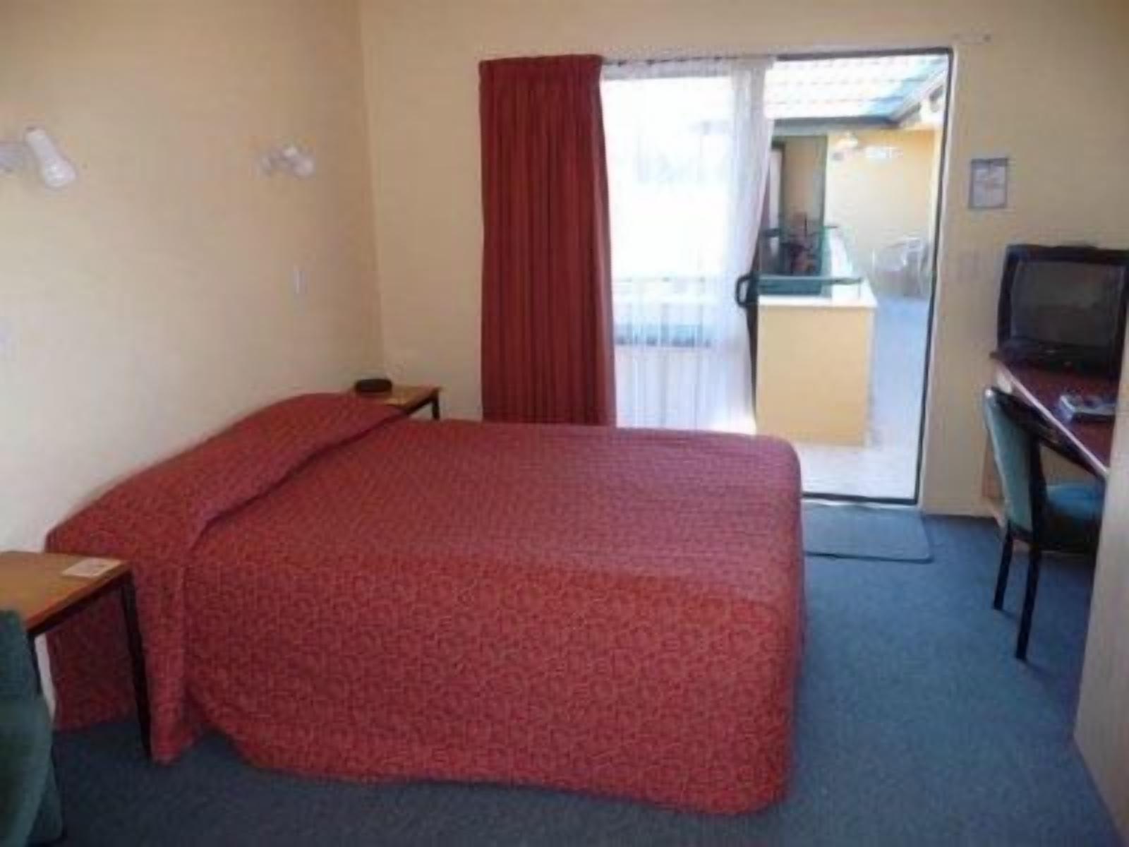 A hotel room with a bed, a desk, a chair, a television, and a sliding door to a balcony.