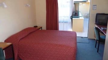 A hotel room with a bed, a desk, a chair, a television, and a sliding door to a balcony.