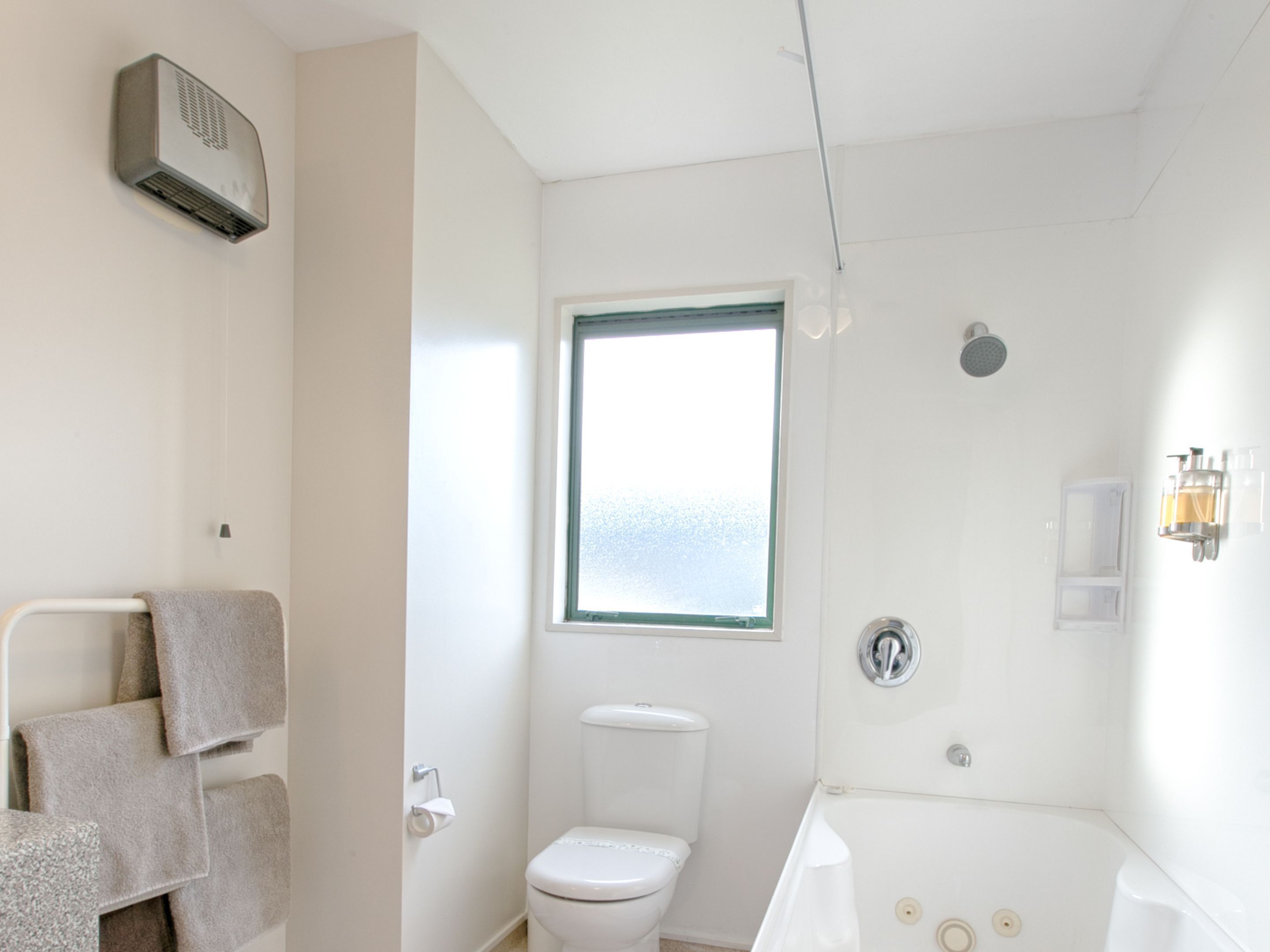 Ein Badezimmer mit Toilette, Fenster, Dusche und Handtuchhalter.