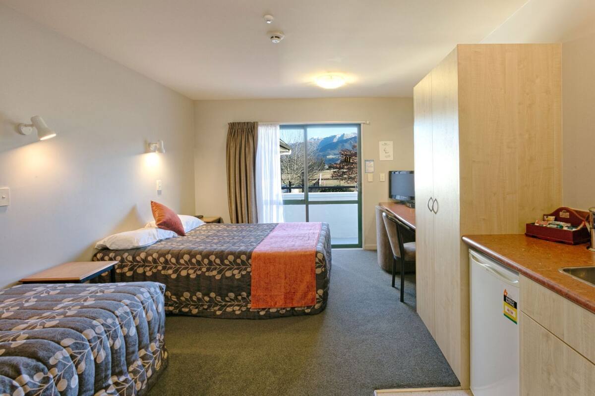 Ein Hotelzimmer mit Bett, einer Sitzecke, einem Schreibtisch, einem Fernseher und Blick auf Berge durch das Fenster.