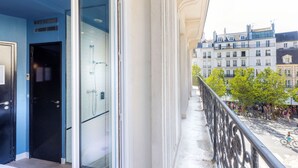 A balcony with a glass door leading to a bathroom, overlooking a street with buildings and people. - Hôtel Emile Le Marais (Paris)