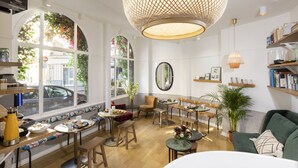 A café with a long counter, seating area, and large windows. - Hôtel Emile Le Marais (Paris)