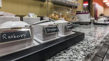 Uma estação de café da manhã com serviço próprio e recipientes identificados para cobertura de framboesa e damasco.