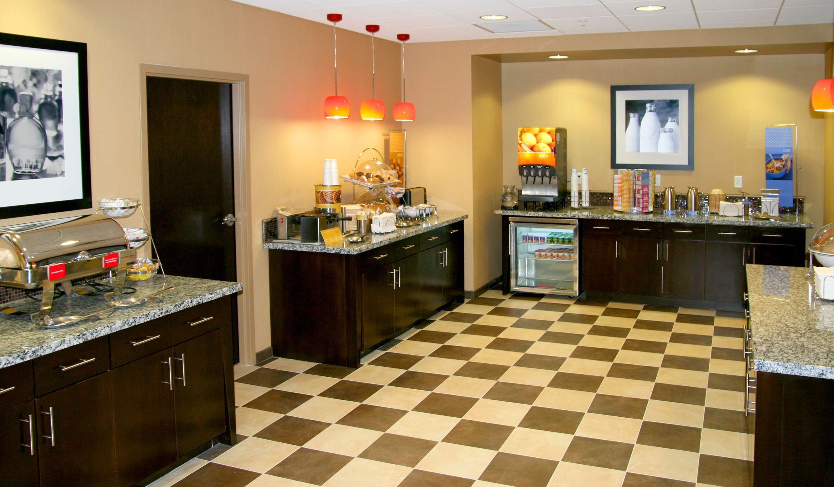 A hotel kitchen with a buffet setup, including a coffee station, a refrigerator, and various food items displayed on the counter.