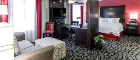 A hotel room with a bed, a desk, a chair, a TV, and a small table.