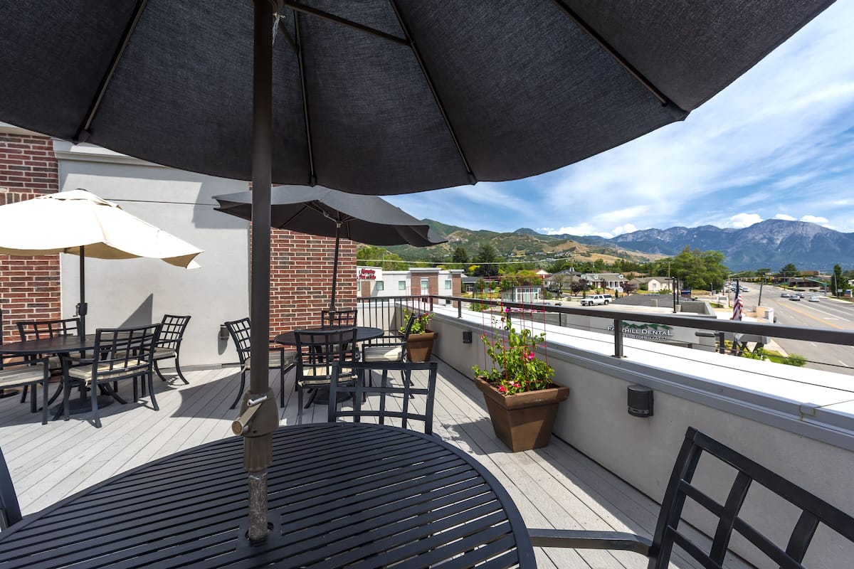 Een terras op het dak met buitenmeubilair, een grote parasol en uitzicht op bergen.