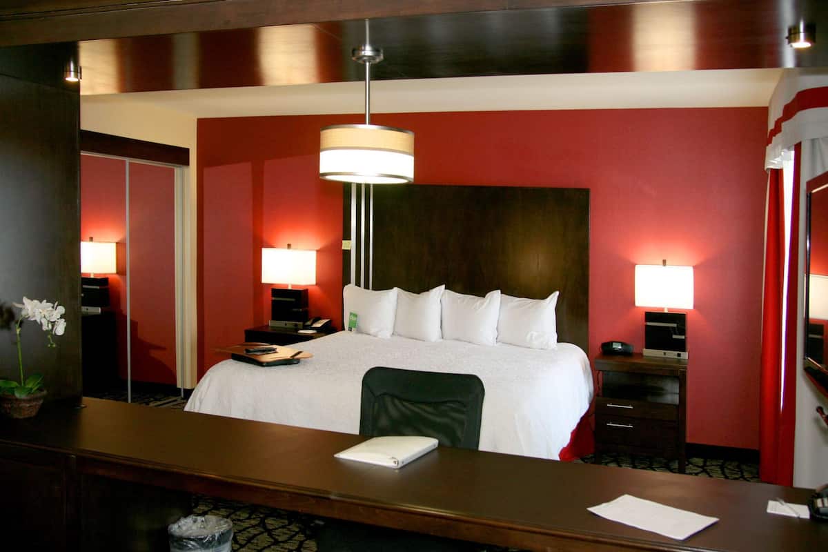 Een hotelkamer met een groot bed, twee nachtkastjes met lampen, een bureau met stoel en een kamerplant.