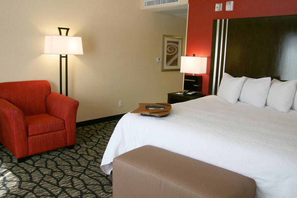 Een hotelkamer met een bed, een rode fauteuil, een nachtkastje met een lamp en een kamerbreed tapijt.