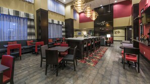 Um restaurante com área de bar, assentos em cadeiras vermelhas e um tapete estampado.