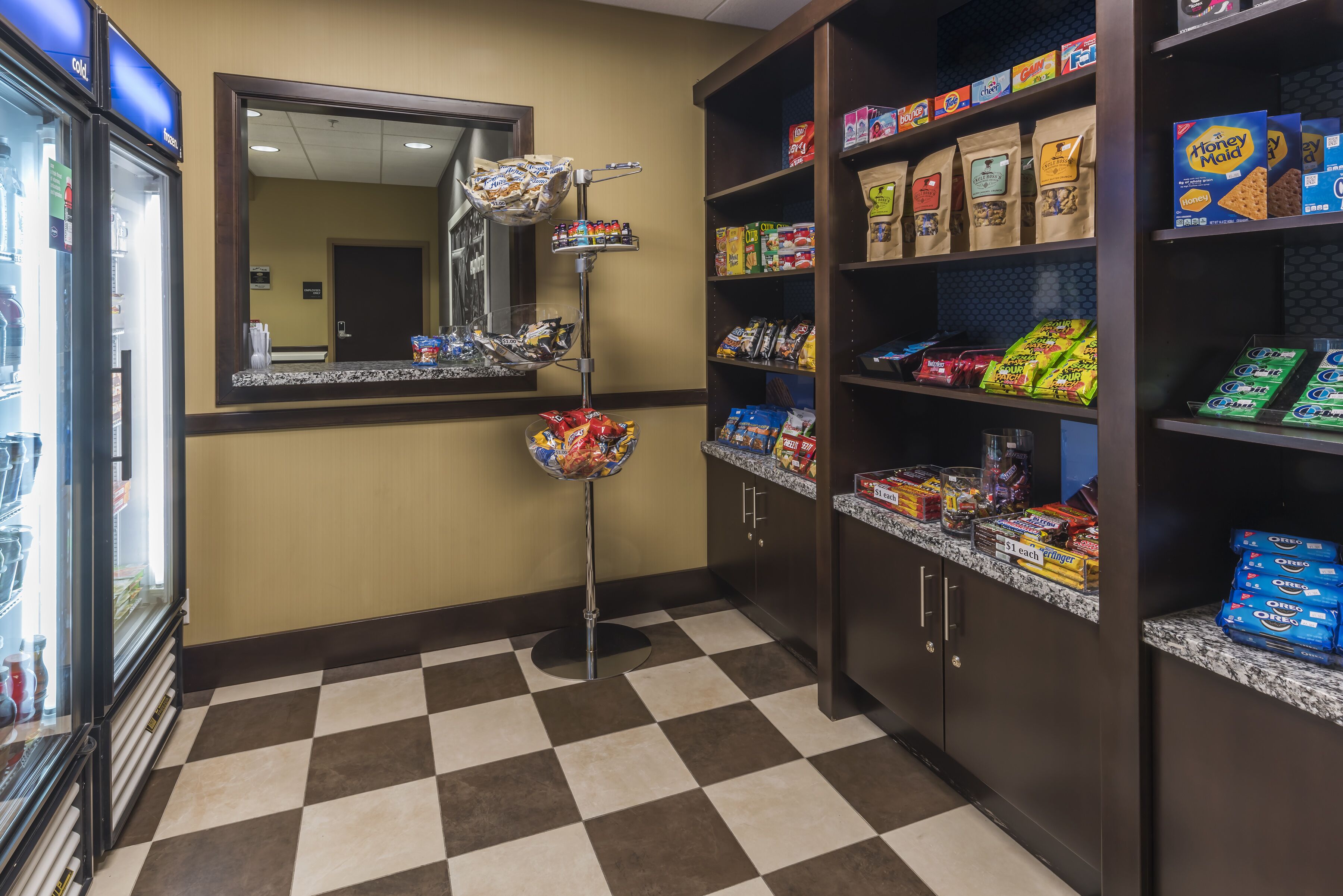 A hotel pantry with shelves stocked with snacks and a refrigerator.