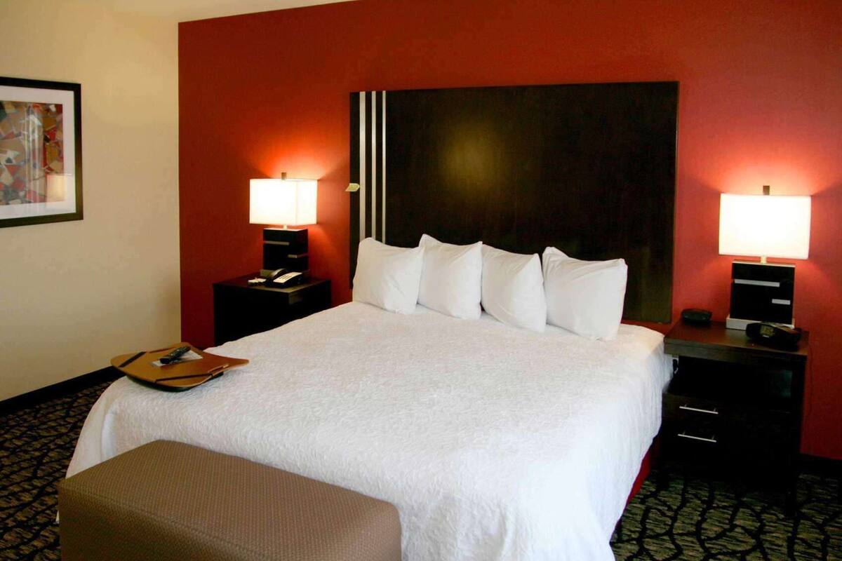 Quarto de hotel com uma cama grande, duas mesas de cabeceira com luminárias, um telefone e uma mesinha com controle remoto.