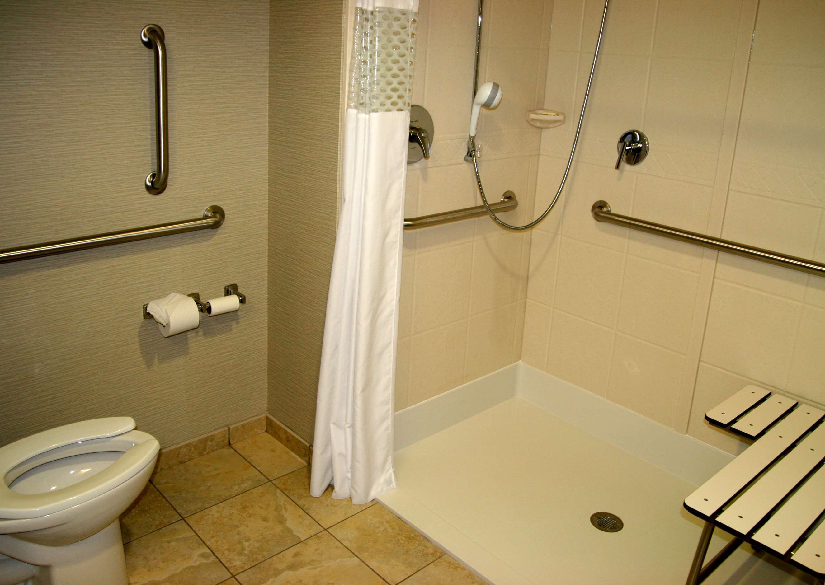 Een badkamer met toilet, douche met glazen deur en een bankje.