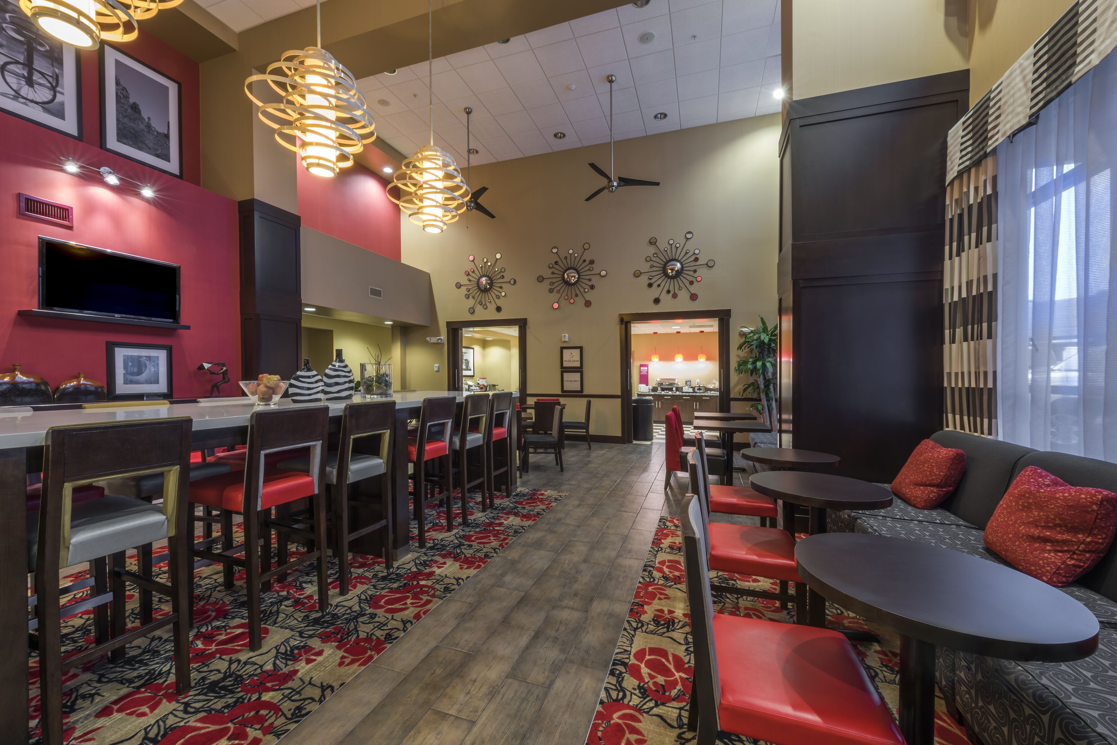 A restaurant with a long counter, multiple chairs, and tables. There are ceiling fans and decorative wall art.