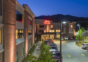 Un hotel con un letrero de neón, un estacionamiento y una montaña al fondo.