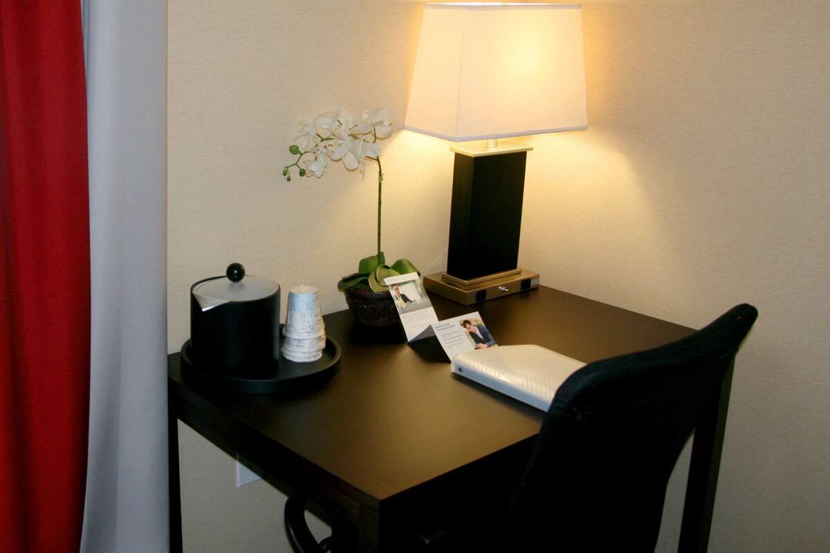 Een bureau in een hotelkamer met een lamp, een potorkidee, een kopje en een notitieboekje.