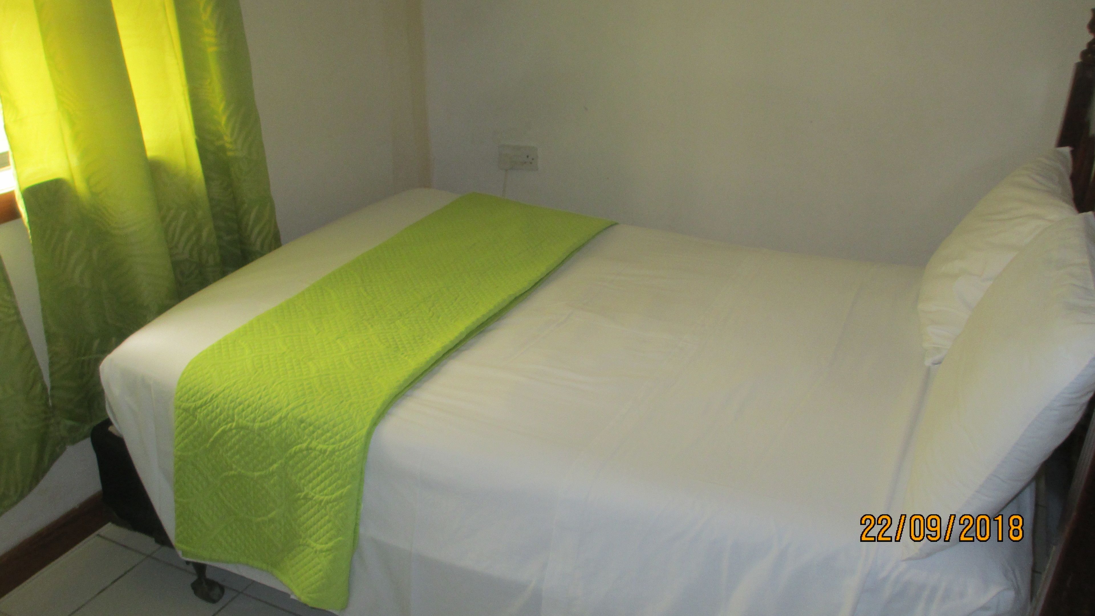 A single-bed room with a green bedspread, white pillows, and a green curtain.