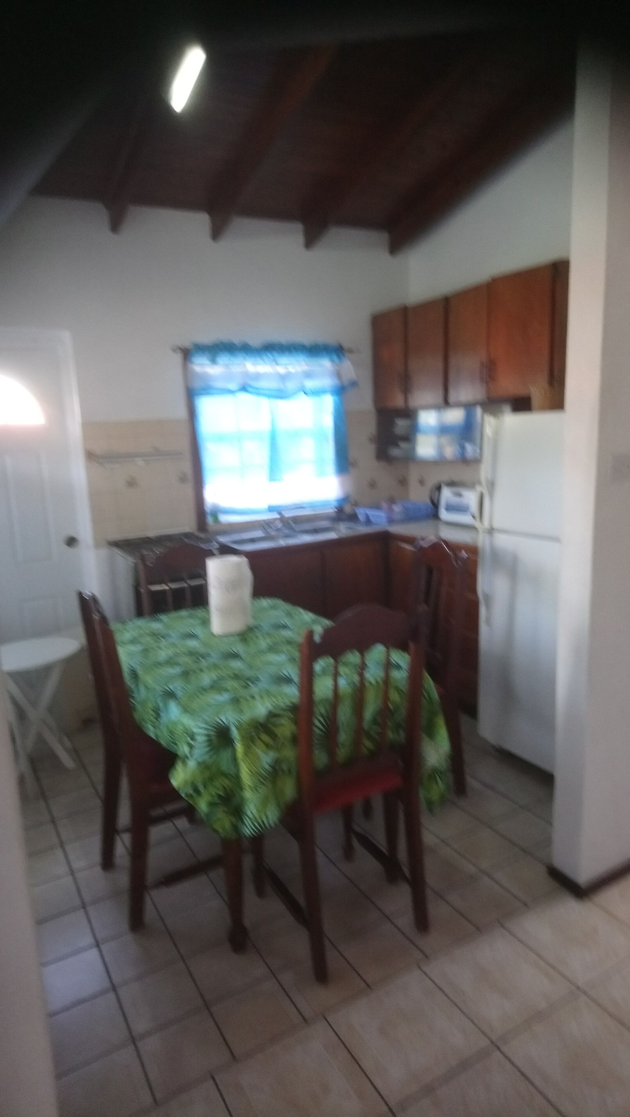 A dining area with a table set for four, a window with blue curtains, wooden cabinets, and a tiled floor.
