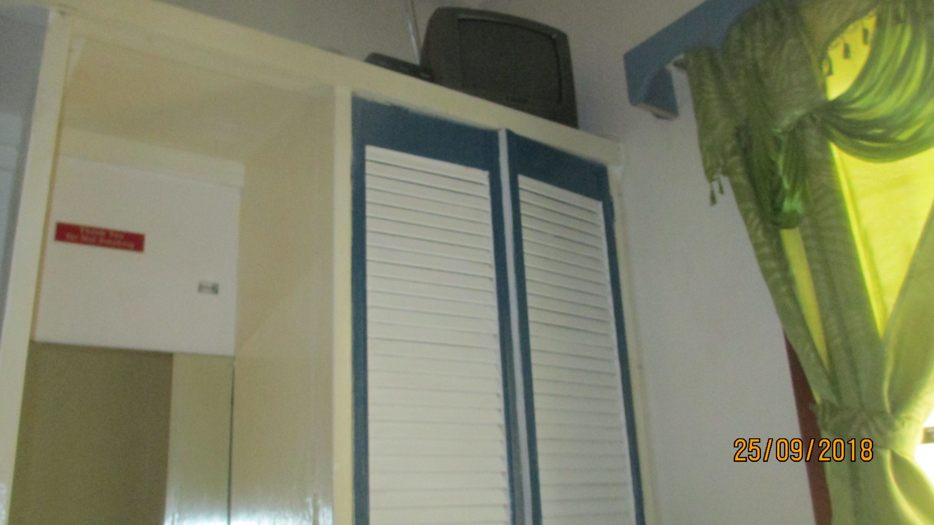 Une pièce avec une porte fermée, une petite télévision posée sur une étagère et un rideau vert.