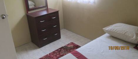 A bedroom with a bed, a dresser with drawers, a mirror, a window with curtains, and a door.