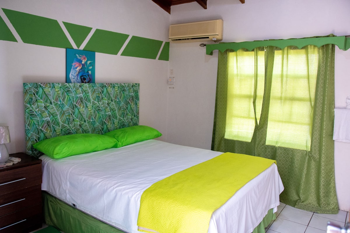 Habitación de hotel con cama, cortinas verdes, un cuadro en la pared y un cabecero verde estampado.
