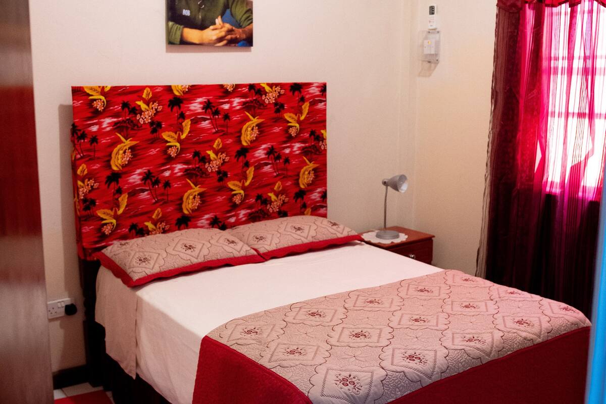 Un dormitorio con una cama, una mesita de noche, un aire acondicionado de pared y un cuadro.