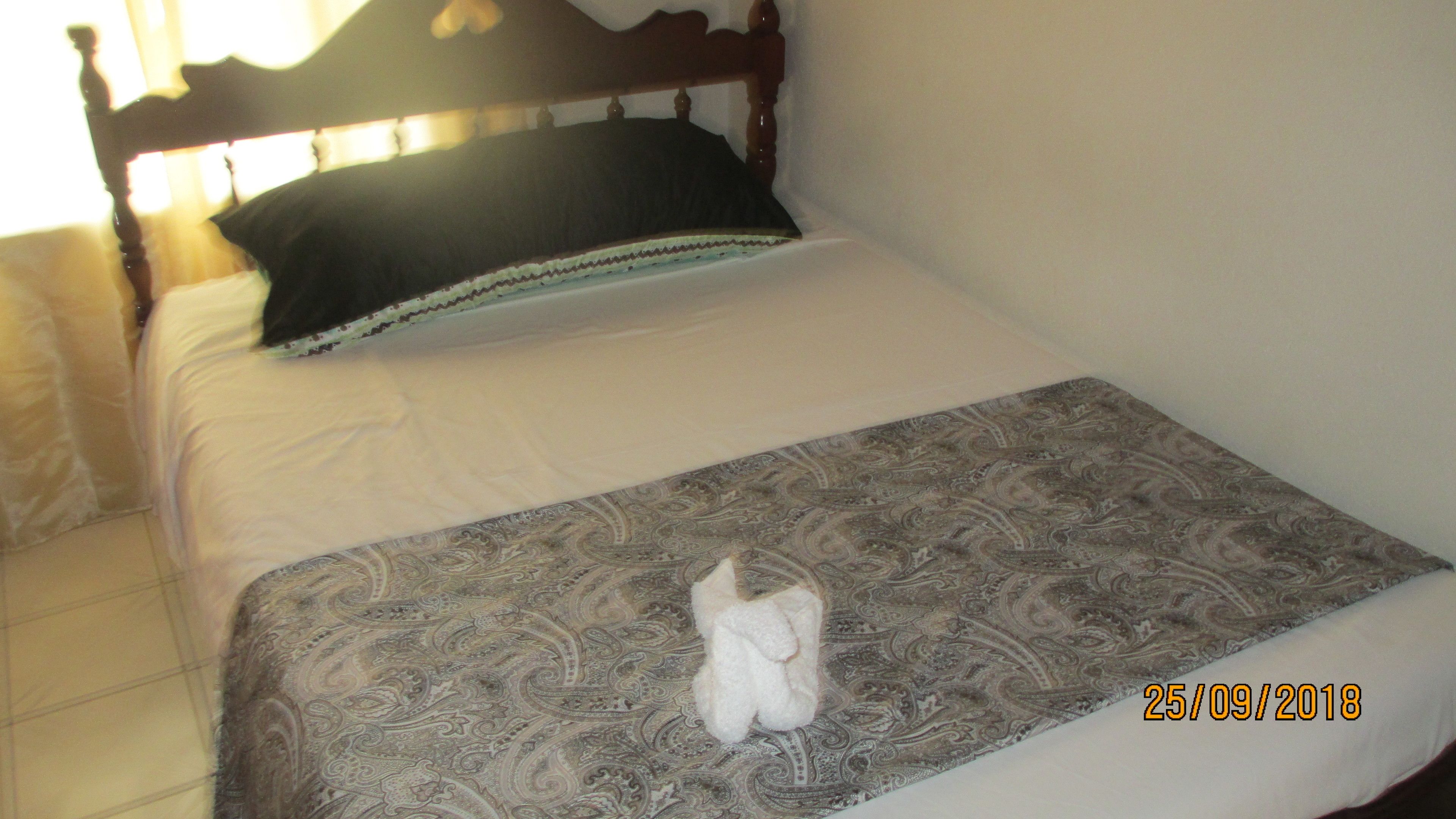 Una cama con una colcha estampada, una almohada y un objeto blanco pequeño sobre la cama.