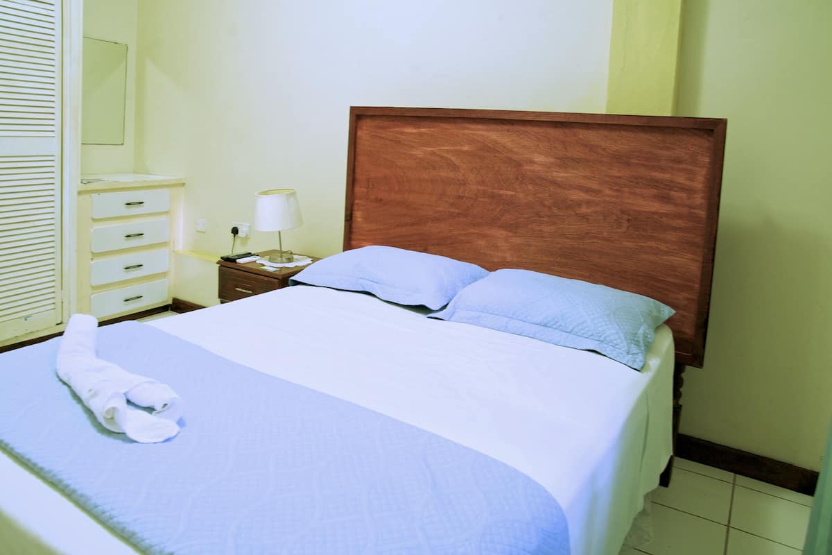 Una cama bien hecha con cabecera de madera, una mesita de noche con lámpara y una toalla doblada sobre la cama.
