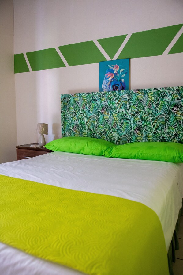 A bed with a green and white bedspread, a green pillow, and a painting of a fish on the wall above the bed.