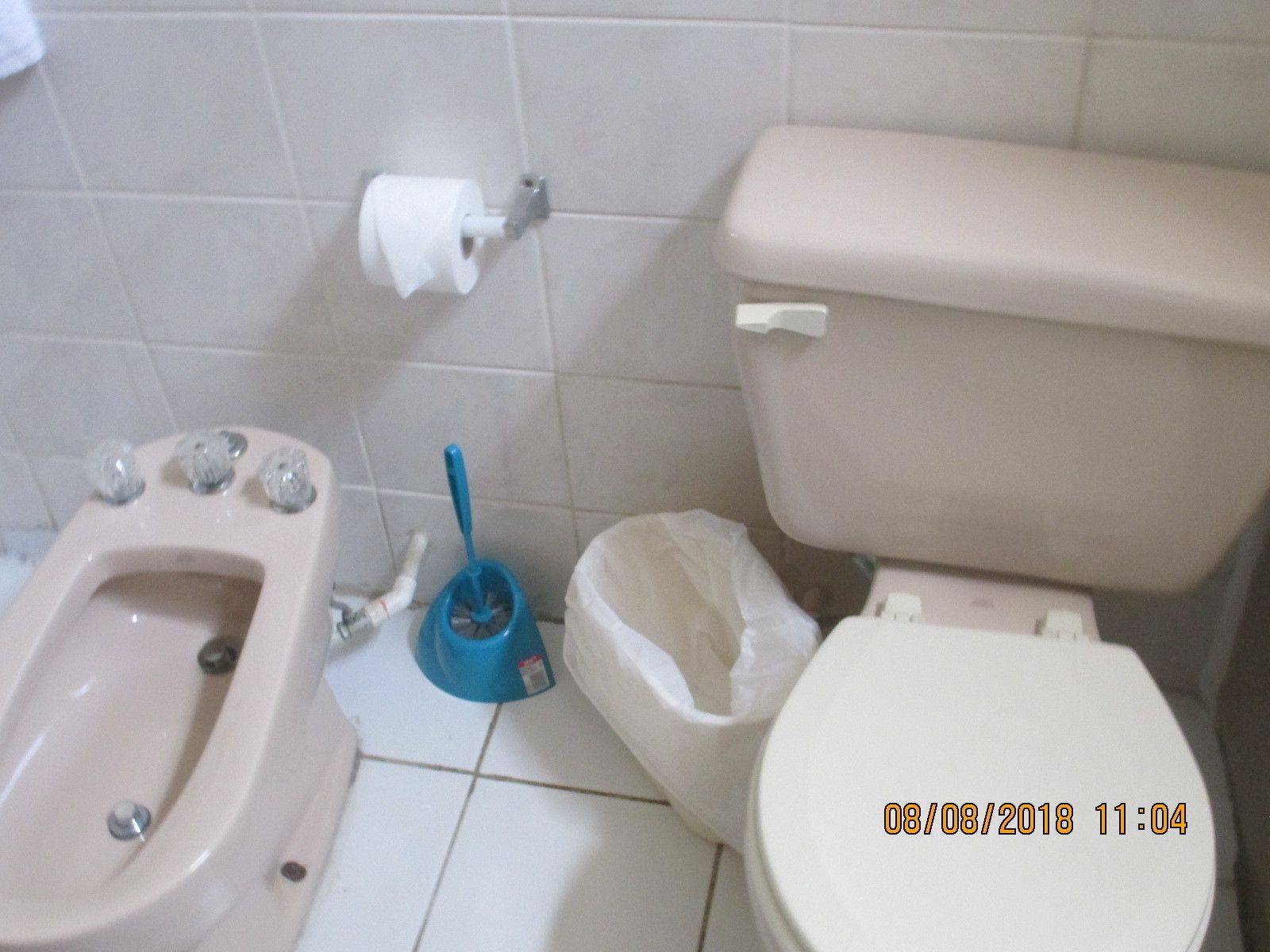 A bathroom with a bidet, toilet, and a blue cleaning brush.
