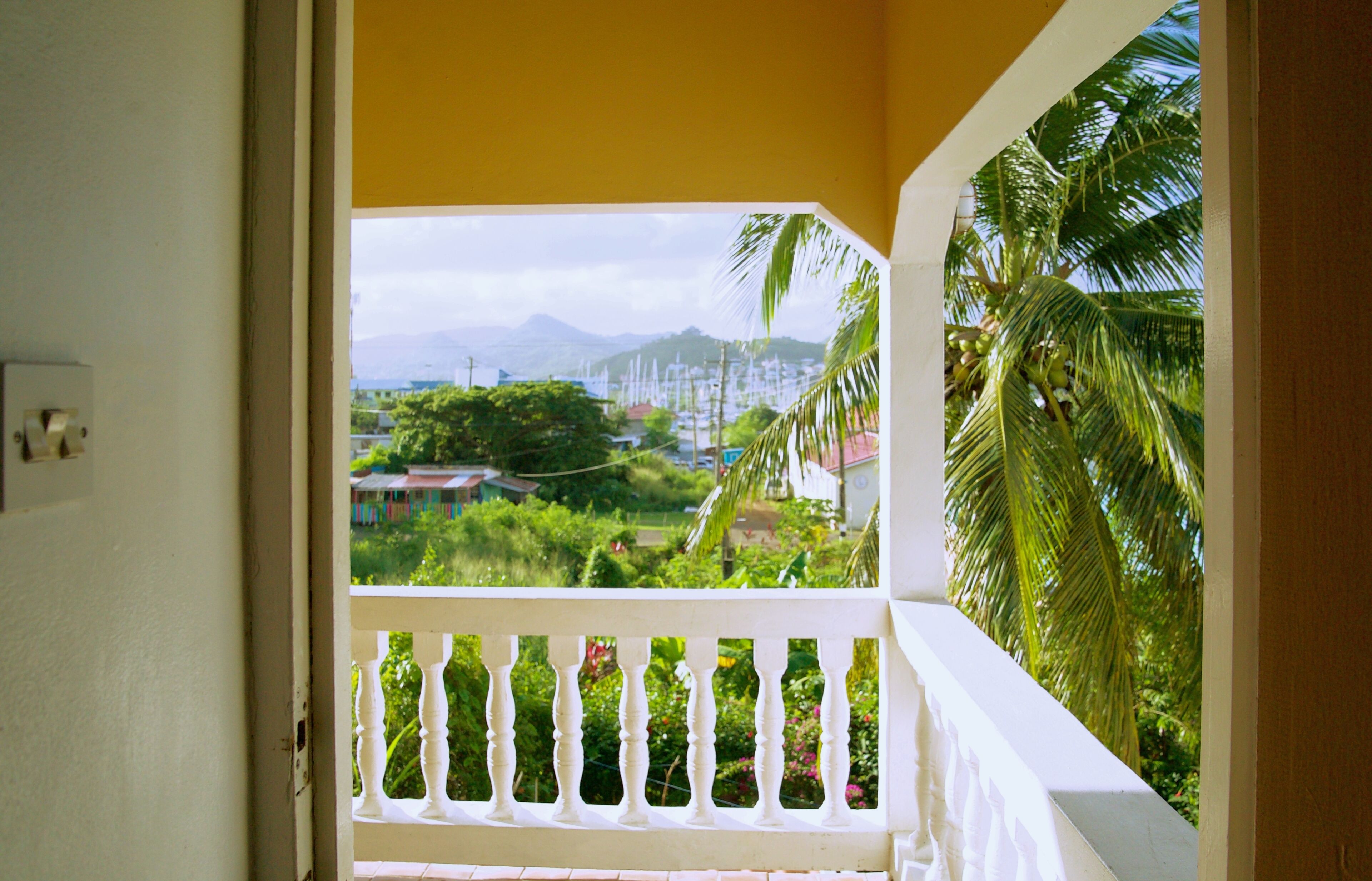 A balcony with a white balustrade overlooking a lush garden and distant mountains.